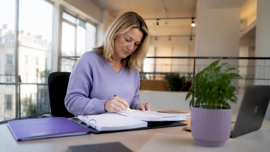 En person sitter vid sitt skrivbord och granskar dokument för att säkerställa att de följer GDPR-regelverket.