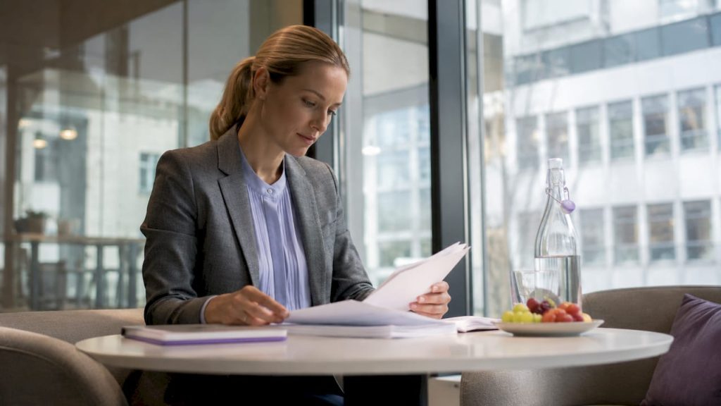 Företagskvinna går igenom regelefterlevnadsdokument vid sitt skrivbord